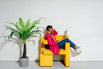 Female freelancer with laptop working in yellow armchair