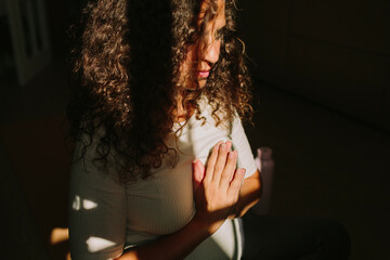 A curly-haired brunette woman meditates in her home