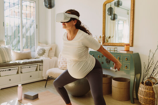 Pregnant brunette woman doing yoga with a VR headset.