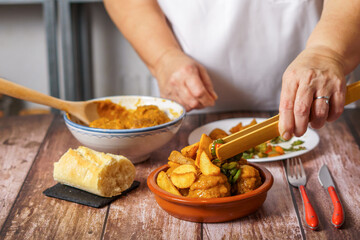 woman in white apron serving potatoes and vegetables over a portion of meatballs