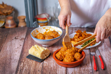 woman in white apron serving meatballs in an earthenware pot