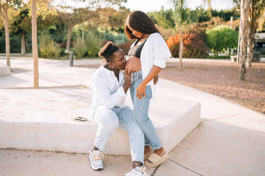 Man kissing belly of pregnant wife in park