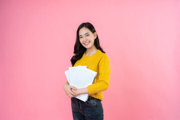 beautiful female student stand gracefully Wears a yellow coat and jeans, has long hair, and has a book in his hand. on the pink background studio High school university college education.