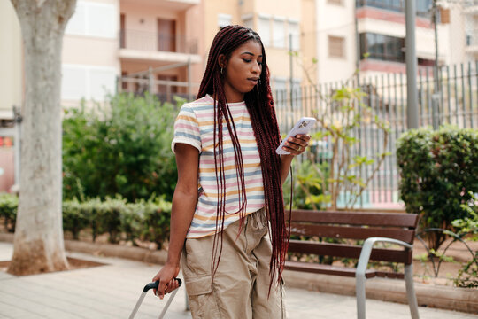 Black woman with suitcase texting on her phone