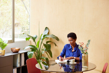 Focused black manager taking notes at table with coffee
