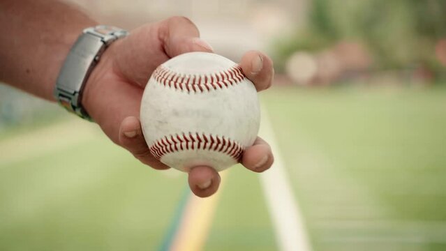 A male baseball hand rotates a ball in his fingers before pitching.  The beautiful dramatic motion is shot in slow motion to capture the gorgeous character of this iconic sports image.