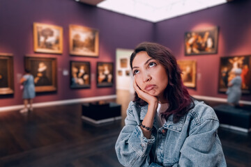 a bored girl visitor or student in an art gallery or museum looks at the masterpieces of classical...