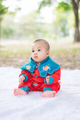 Portrait of a five-month-old Asian baby boy in a Chinese costume sitting and yawning on a white mat with a bokeh background in a park. cute baby boy.