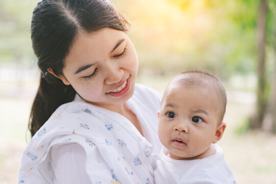 Asian Mothers Or Single Moms Are Smiling And Hugging Newborn Babies. Family Doing Activities And Relaxing In The Park. Concepts About The Duties Of A Wife And Mother In Raising Children And Family.