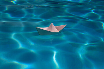 Paper boat sailing on water causing waves and ripples. Paper boat into water. Concept of tourism, travel dreams vacation holiday, dreaming traveling, sailing adventure. Paper art style.