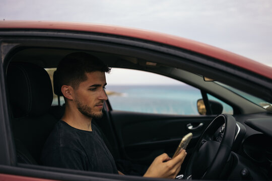 Man using the mobile in the car parked in front of the sea