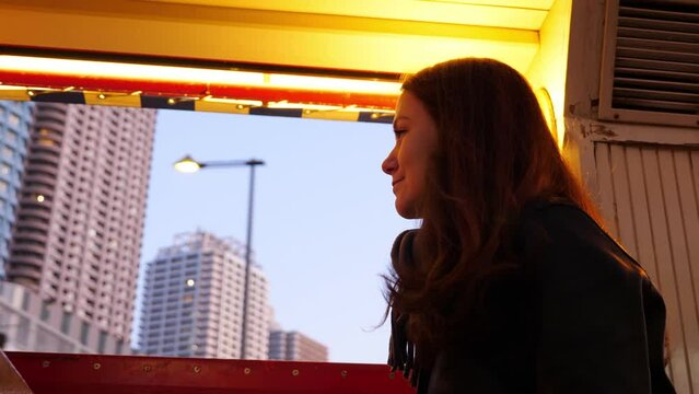 Tourist woman enjoy evening time cruise at Sumida river by waterbus. Side portrait shot, from low angle, blurred city buildings seen on background. Passenger looking at scenic Tokyo views from water