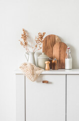 Cozy kitchen interior. Dishes, cutting boards, a jug of dried flowers on a white cabinet