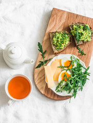 A simple healthy breakfast - boiled egg, arugula salad, avocado sandwich and tea on a light background, top view