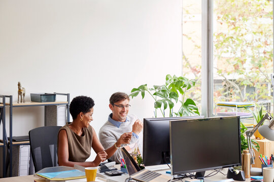 Positive diverse coworkers smiling at desk in office