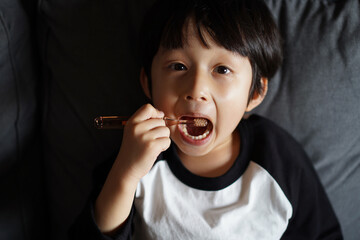 Little Asian boy, brushing his teeth on the sofa 