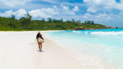 Young Asian woman with a hat walking at a tropical beach, Anse Cocos beach La Digue Seychelles...