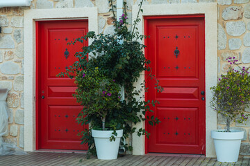 traditional  stone  Greek house facade with  red doors . Close-up of a wooden blue  dors and flower in a white stone building