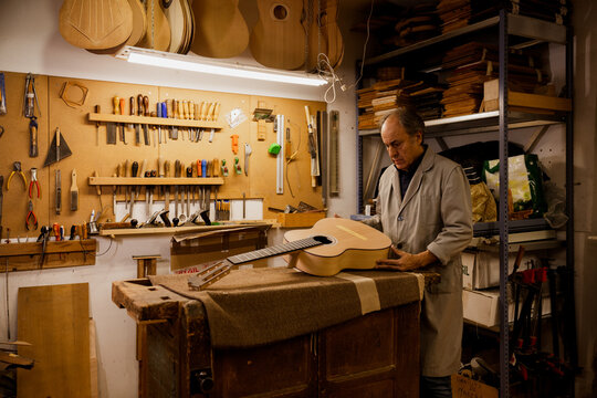 Focused luthier working in workshop with a classic spanish guitar