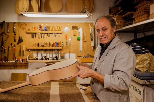 Smiling senior carpenter with tools in luthier workshop
