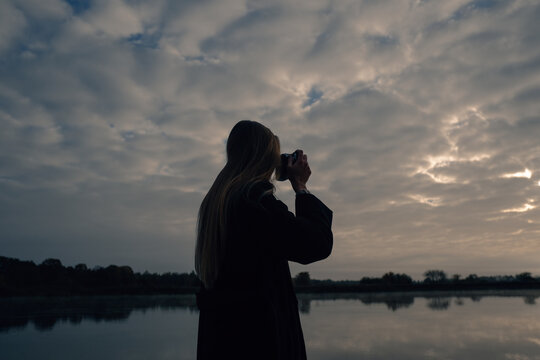 Silhouette of a girl photographing the sunrise on the river