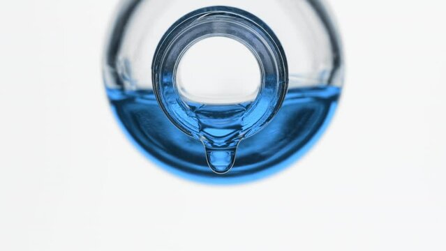 Side view macro shot of blue oil is dripping from reagent bottle on grey background | Abstract skin nutrition cosmetics ingredients formulating concept