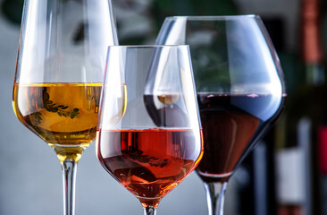 Red, white, rose wine glasses on gray background. Wine bar, shop, tasting concept. Wines and bottles in assortment