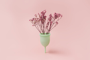 In a green menstrual cup, dry red flowers against a pink background.