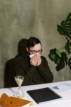 man blowing his nose at his desk