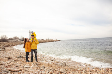 Happy multinational family walking in the beach with little kid tigether in cold weather against the background sea