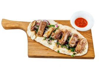 Fried ribs with sauce, herbs and onions on a flatbread served on a wooden board. Appetizing popular dish of oriental cuisine. Top view. Close-up. Isolated on white background.