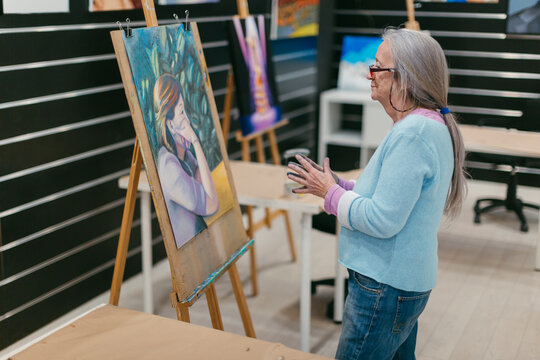Grey-haired woman with glasses in art school  analyzing her artwork