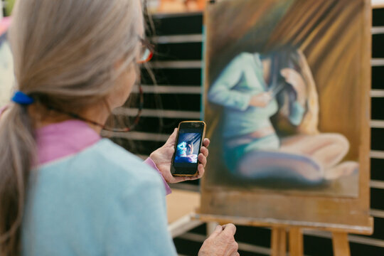 Painter comparing artwork with reference picture on smartphone 