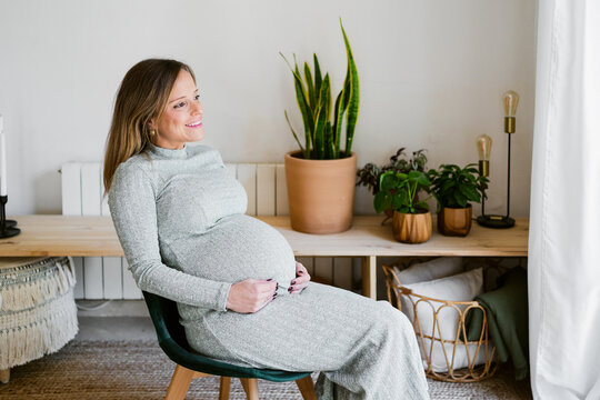 Expectant woman relaxing touching her belly at home