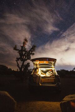 Woman Relaxing Under Night Sky In Joshua Tree With Car Camper