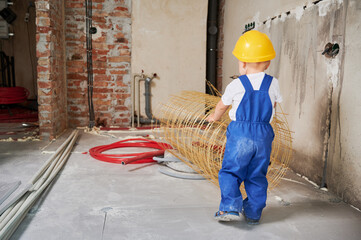 Back view of baby boy in safety helmet using mesh fiberglass rebar for home renovation. Child...