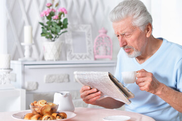 Emotional senior man reading newspaper at home