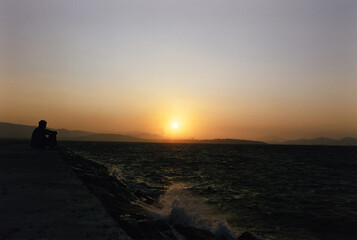 Silhouette of Man Sitting By Water and Watching Sunset