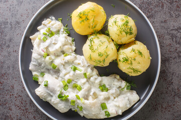 Spicy herring fillet in a creamy sauce with a garnish of boiled potatoes close-up in a plate on the...