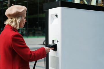 Woman plugs cable into electric car charging station