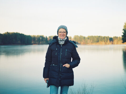 Smiling Middle Aged Woman Standing By A Lake In Winter