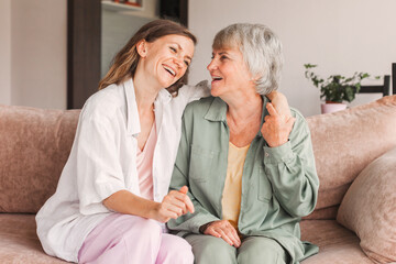 Older mature mother and grown millennial daughter laughing embracing, caring smiling young woman embracing happy senior middle aged mom