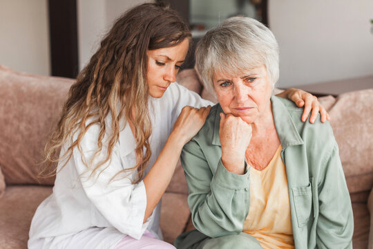 Grown up daughter soothe aged mother holds her hand feel empathy give her moral support, sad elderly woman at home