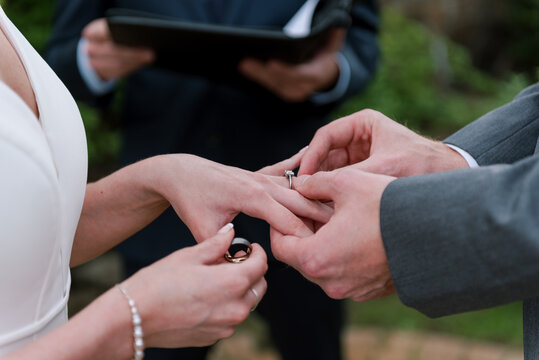 man in suit putting wedding ring on his wife's finger at wedding