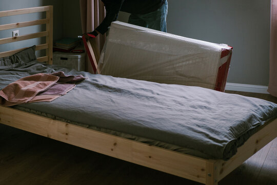 Adult man unpacking new heating radiator next to wooden bed 