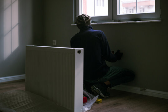 A male worker makes a marking for the heating system in an apartment