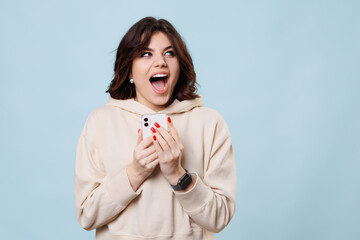 A pretty teenager in a studio shot, laughing and looking at camera joyful as she shops, smartphone.