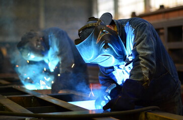 Workers wearing industrial uniforms and Welded Iron Mask at Steel welding plants, industrial safety first	