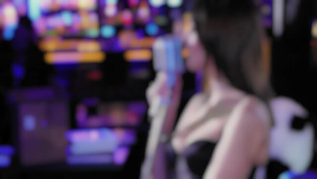 Sexy girl sings into steel chrome vintage microphone in cabaret bar or karaoke night club during jazz show on stage, blurred. Female artist woman performs at corporate party or pop concert. Song voice