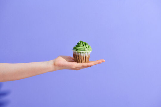 cropped image of girl holding cupcake in hand isolated on purple